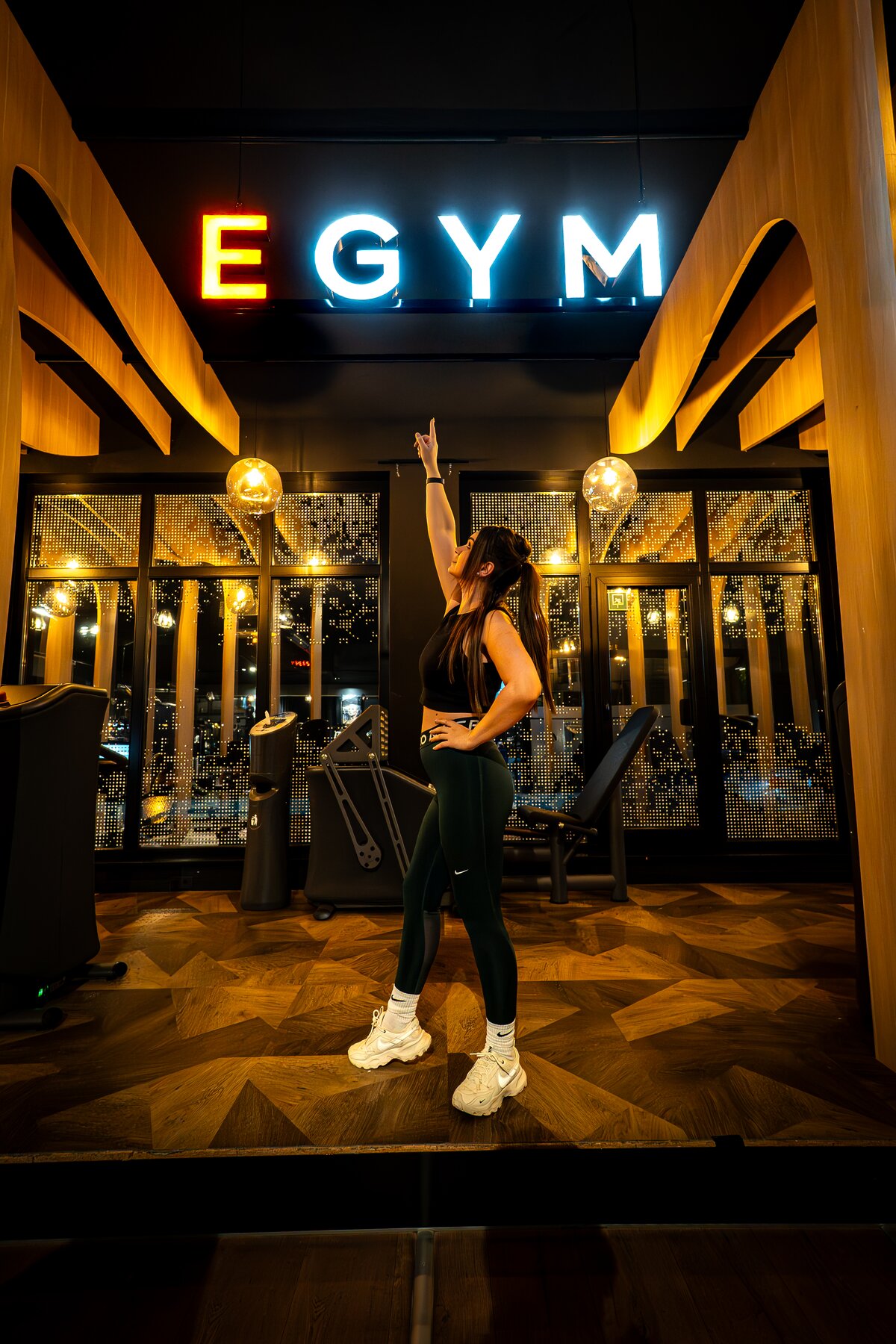Sportlerin posiert unter leuchtendem EGYM Neon-Schriftzug im Fitnessstudio Bitburg GymOne 24/7